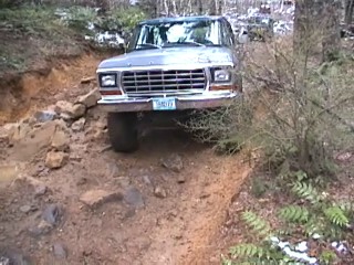 1979 Ford Bronco - This 1979 Ford Bronco navigates a challenging off-road trail, with trees and foliage surrounding the muddy path.