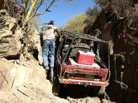 1987 Suzuki Samurai - A red 1987 Suzuki Samurai navigates a narrow, rocky trail with a person climbing out.