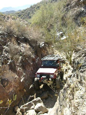 1987 Suzuki Samurai - A red 1987 Suzuki Samurai navigates a challenging rocky terrain, its off-road capabilities.