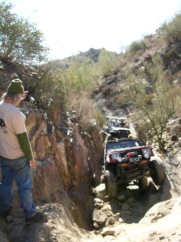 1987 Suzuki Samurai - Multiple off-road vehicles tackle a challenging, narrow, rocky trail in a desert environment.