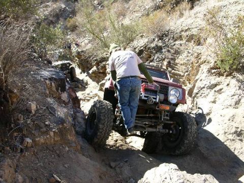 1987 Suzuki Samurai - A red 1987 Suzuki Samurai navigates a steep, rocky trail with large off-road tires.