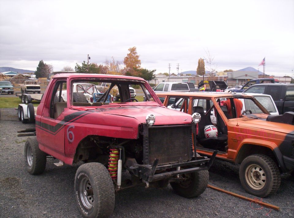 Modified red pickup truck with roll cage and orange SUV parked side-by-side
