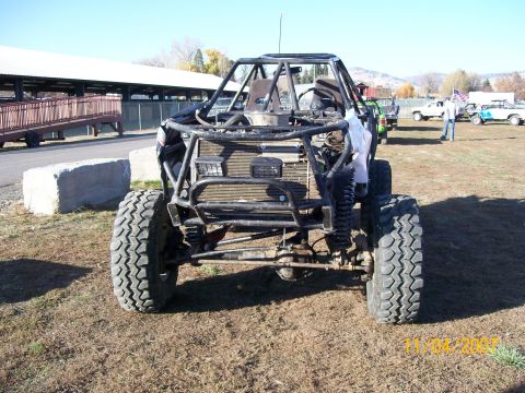 1984 Ford Bronco - A heavily modified off-road vehicle with a prominent roll cage sits in a grassy field.