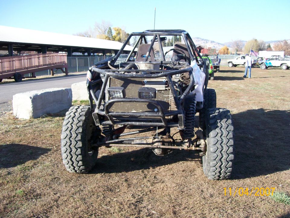 Custom buggy with roll cage, large tires, and exposed engine bay. Other trucks visible in background