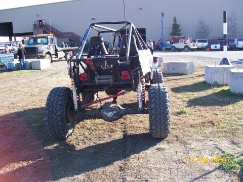 1984 Ford Bronco - Modified off-road vehicle with a roll cage and winch is seen from the rear at an outdoor event.