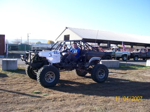 1984 Ford Bronco - Custom off-road buggy with a roll cage and large tires is seen at an event, with other trucks in the background.