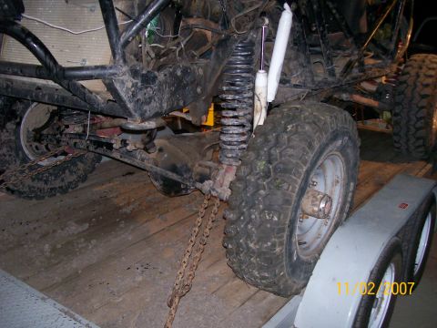 1984 Ford Bronco - Close-up of off-road vehicle suspension and tire, secured with chains on a trailer.