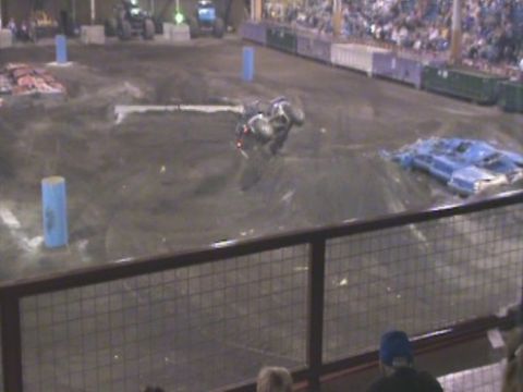 1984 Ford Bronco - A monster truck is overturned on a dirt arena during a show, with a crowd watching.