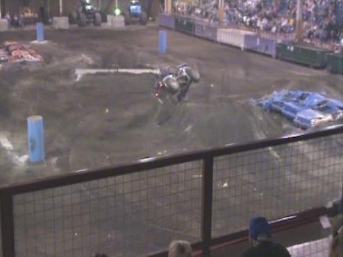 Monster truck upside down on dirt track with spectators in background