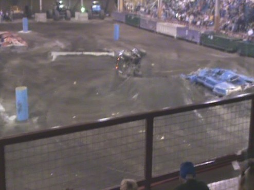 Demolition derby arena with damaged vehicles and spectators in background
