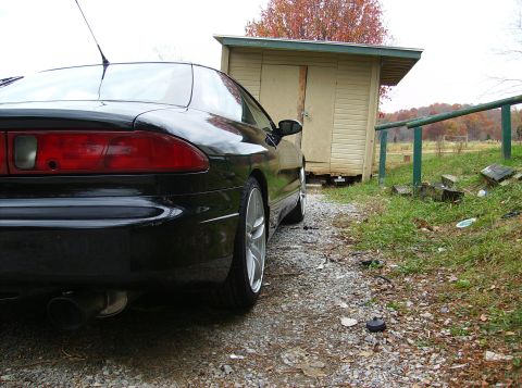 1995 Ford Probe - Rear view of a black 1995 Ford Probe GT parked on a gravel driveway near a wooden shed.