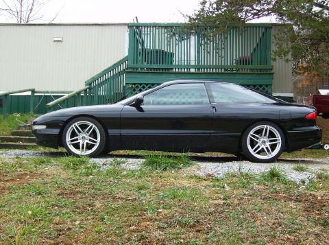1995 Ford Probe - Side view of a black Ford Probe with aftermarket wheels parked on a gravel driveway.