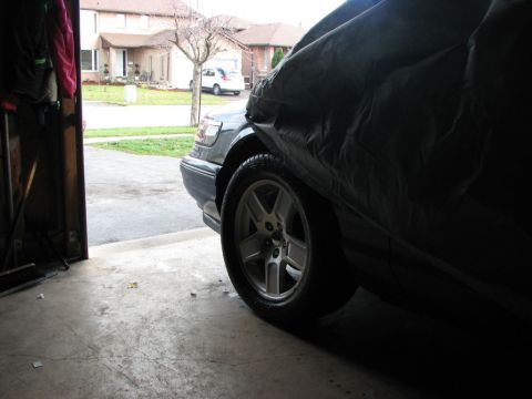 1985 Mercury Grand Marquis - A car is partially covered by a tarp inside a garage, with a residential street visible outside.