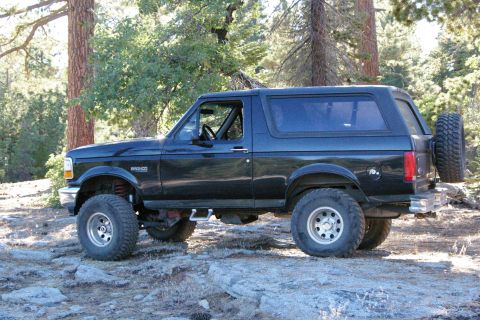 1996 Ford Bronco - A black 1996 Ford Bronco is parked on a rocky trail surrounded by trees.