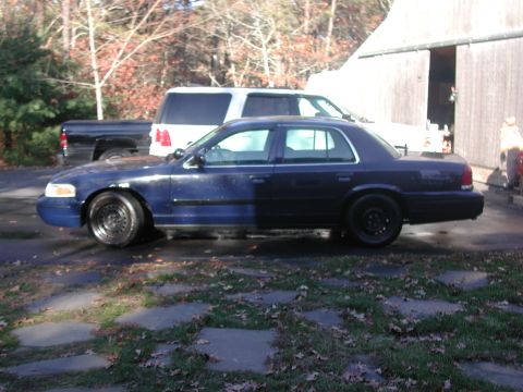 1999 Ford Crown Victoria - A dark blue 1998 Ford Crown Victoria is parked next to a white SUV and a black pickup truck.