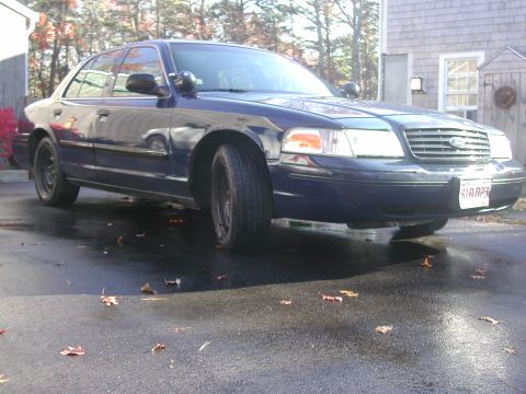 1999 Ford Crown Victoria - Dark blue Ford Crown Victoria parked on wet asphalt with fallen leaves.