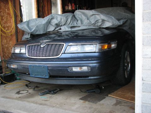 1985 Mercury Grand Marquis - A dark blue sedan, likely from the early 1990s, is parked indoors and covered with a grey car cover.