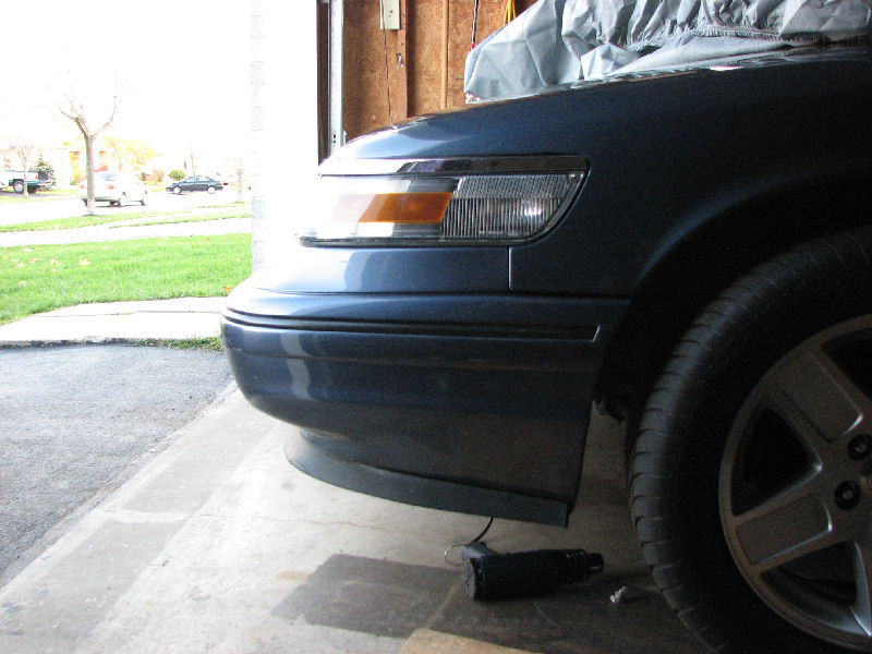 Front corner of a blue-gray sedan in a garage with an impact wrench on the floor