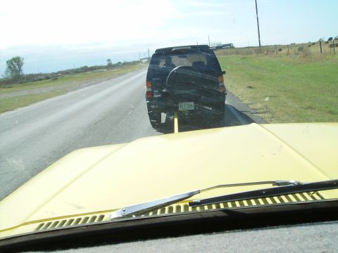 1979 Ford F-100 - View from a yellow vehicle's hood shows a black SUV ahead on a rural highway.