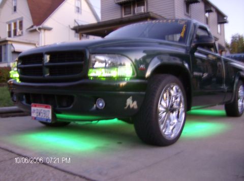 1970 Ford Ranchero - A dark green pickup truck with custom green underglow lighting and chrome wheels is parked on a driveway.