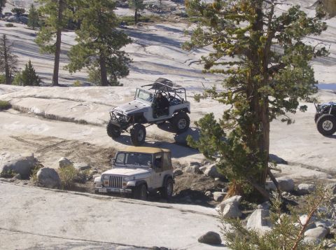 1986 Ford Bronco - Off-road vehicles traverse a challenging rocky terrain under a clear sky.