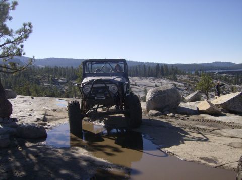 1986 Ford Bronco - Off-road vehicle navigating challenging terrain with puddles and large rocks.
