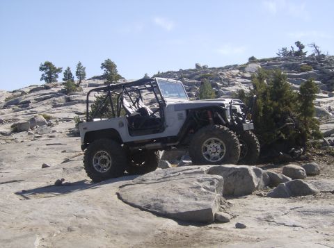 1986 Ford Bronco - This heavily modified SUV navigates a rocky, mountainous landscape under a clear blue sky.