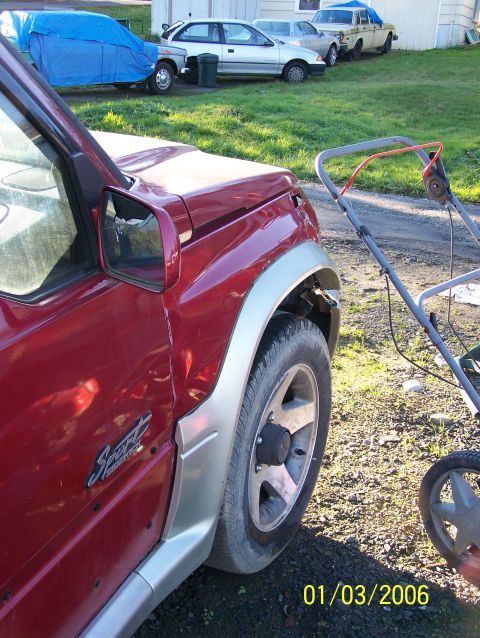 1988 Suzuki Samurai - A red SUV is parked next to a lawnmower, with other vehicles visible in the background.