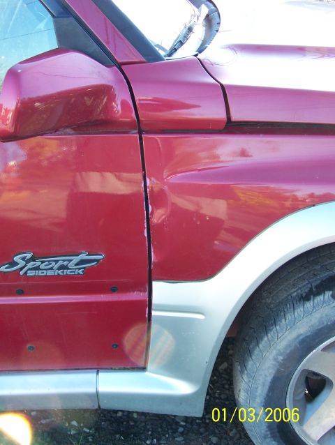 1988 Suzuki Samurai - Close-up of a red Suzuki Sidekick Sport showing damage to the front fender and door.