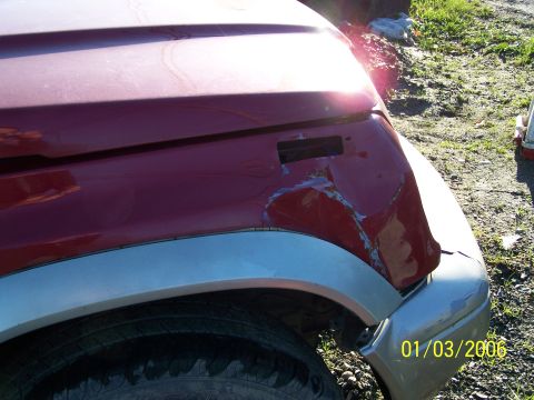 1988 Suzuki Samurai - The front fender of a red SUV shows significant damage, with a silver trim piece and tire visible below.