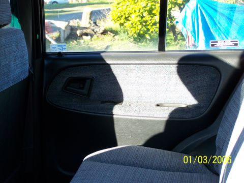1988 Suzuki Samurai - View of the interior door panel and seat, with a window looking out onto a yard.
