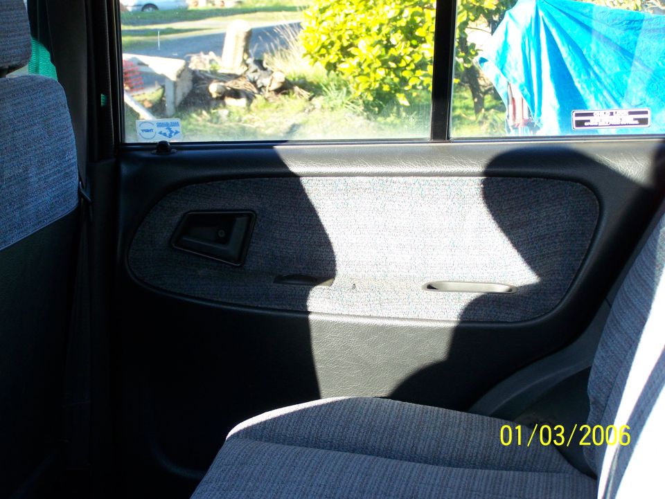 Interior door panel and seat of a vehicle, with a window showing outdoor scenery and a blue tarp