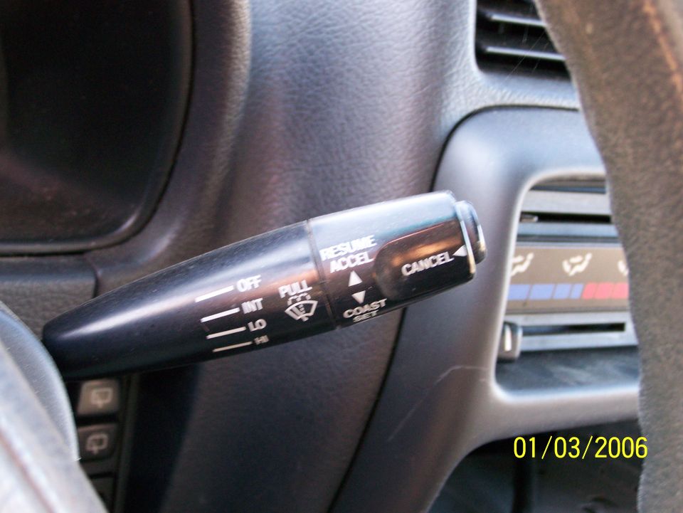 Close-up of a car's interior, focusing on the windshield wiper control stalk with labels like OFF, INT, LO, HI, PULL, RESUME, ACCEL, and CANCEL. The date 01/03/2006 is visible