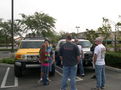 2007 Toyota FJ Cruiser - Two Toyota FJ Cruisers, one yellow and one silver, are parked side-by-side in a lot while a group of people converse.