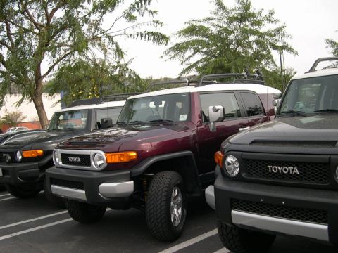 2007 Toyota FJ Cruiser - Multiple Toyota FJ Cruisers are parked in a lot. The middle vehicle is maroon with a white roof, and two black FJ Cruisers are on either si…