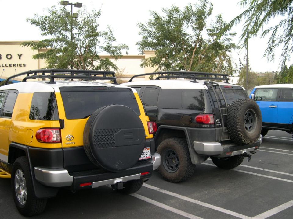 Yellow 2007 Toyota FJ Cruiser parked next to a black one, with a blue one in the background