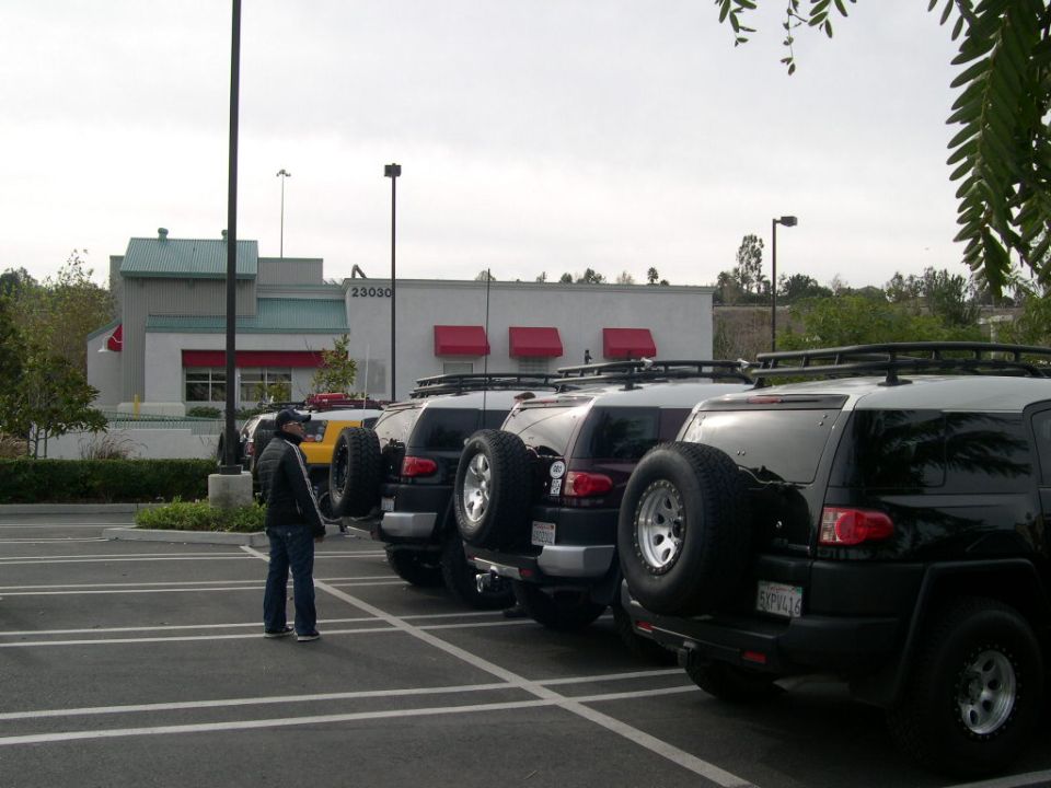 Several black Toyota FJ Cruisers parked in a lot. One person stands nearby