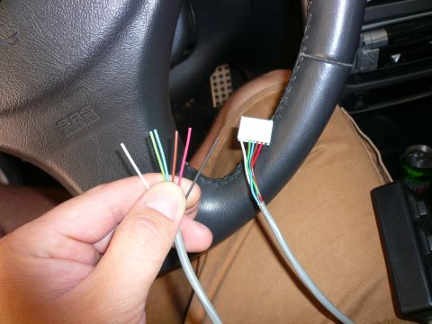 1996 Ford Probe - A hand holds several wires near the steering wheel of a vehicle, with the SRS airbag text visible.