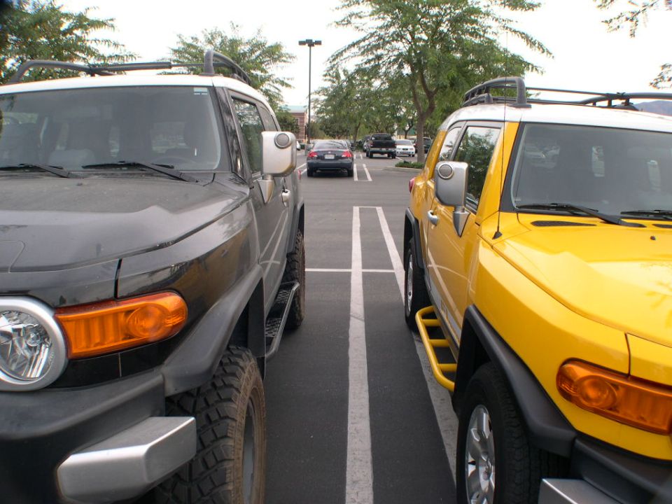 Two Toyota FJ Cruisers, one black and one yellow, parked in adjacent parking spots