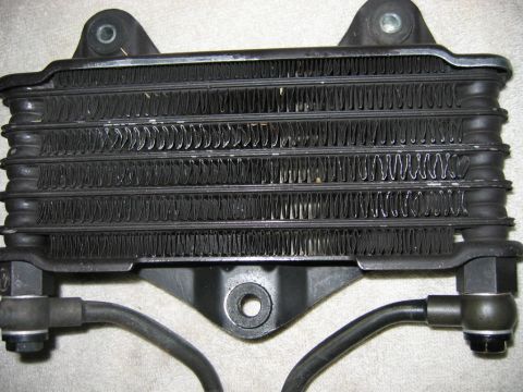 1985 Ford LTD Crown Victoria - A black metal oil cooler with multiple rows of fins and two hoses is shown from the front.