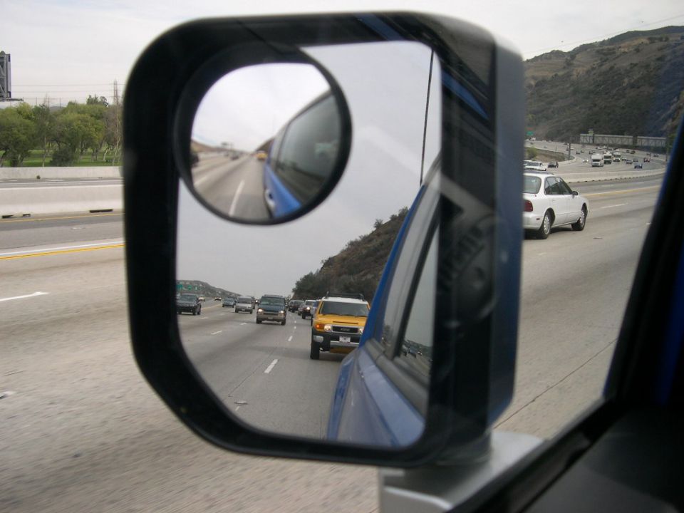 Highway traffic including a yellow SUV and a white sedan, seen in a side mirror