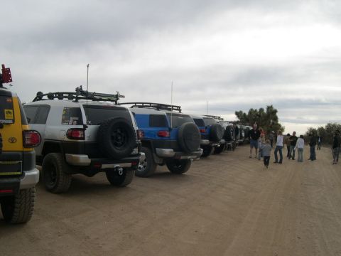 2007 Toyota FJ Cruiser - A group of off-road vehicles are lined up on a dusty trail under a cloudy sky.