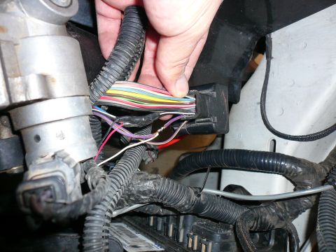 1996 Ford Probe - A close-up view of a vehicle's electrical wiring harness and connectors, with a hand disconnecting a plug.