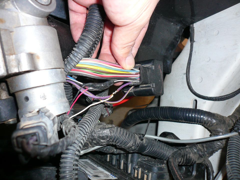Hand disconnecting a multi-colored wire harness connector in a vehicle's engine bay