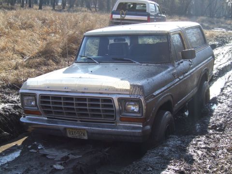 1979 Ford Bronco - Two Ford Broncos navigate a muddy trail, with one vehicle deeply mired in the muck.