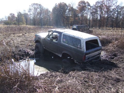 1979 Ford Bronco - A Ford Bronco is stuck in the mud off-road, with another vehicle visible in the distance.