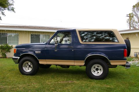 1986 Ford Bronco - Side view of a 1986 Ford Bronco, showing its blue body and tan removable top.