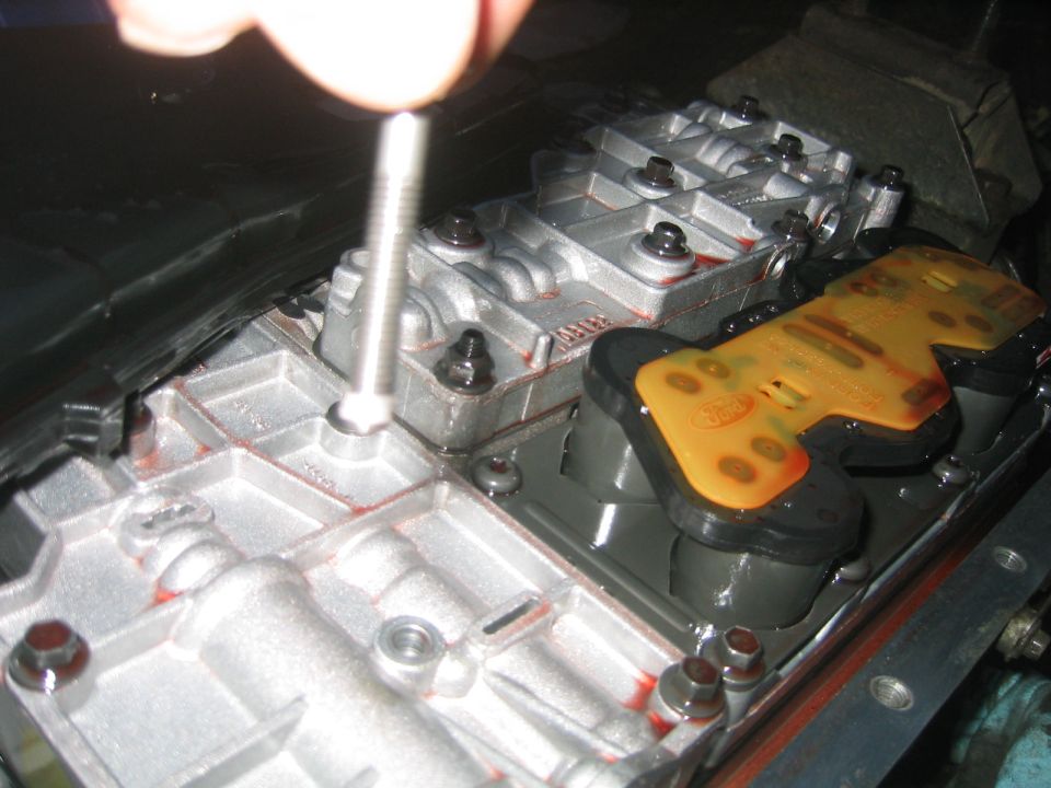 Hand removing bolt from automatic transmission valve body with yellow Ford solenoid block