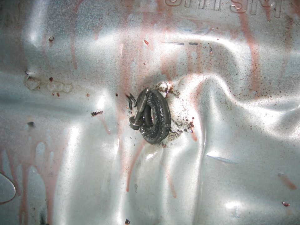 Close-up of a transmission pan with a bolt and some red fluid drips