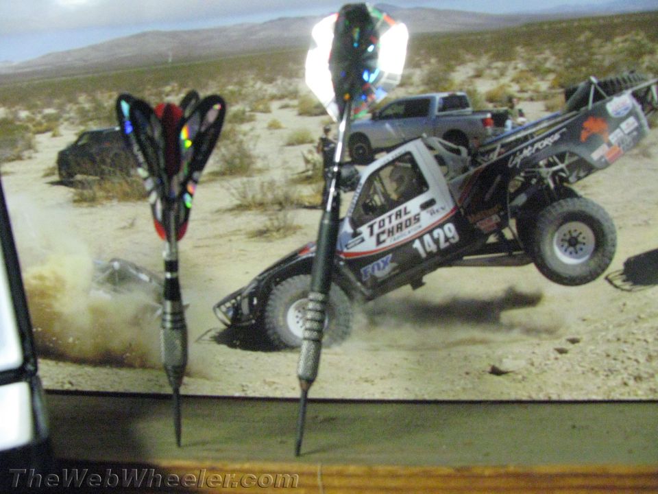 Two darts in foreground with a desert racing truck jumping in background